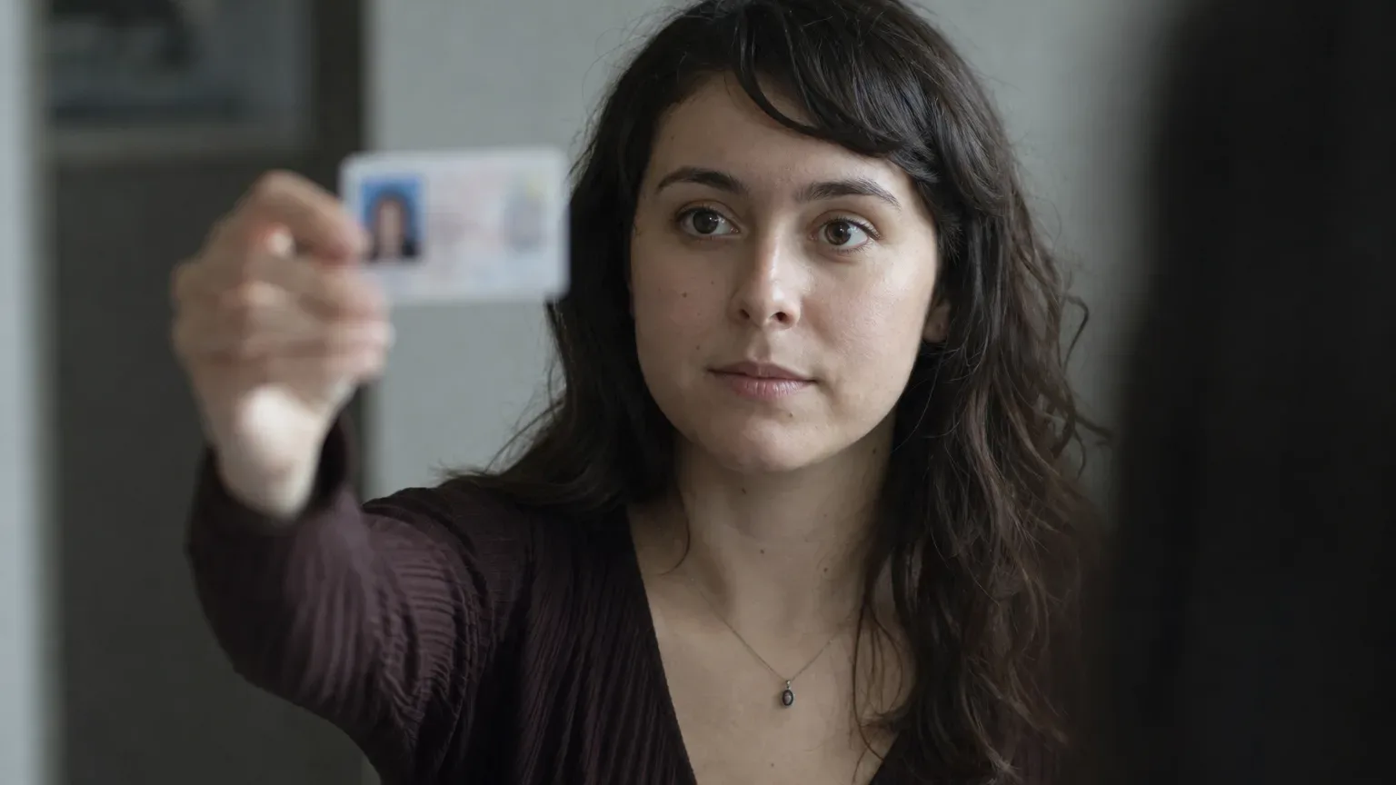 A person holding up a driver's license at eye level as if presenting it for inspection