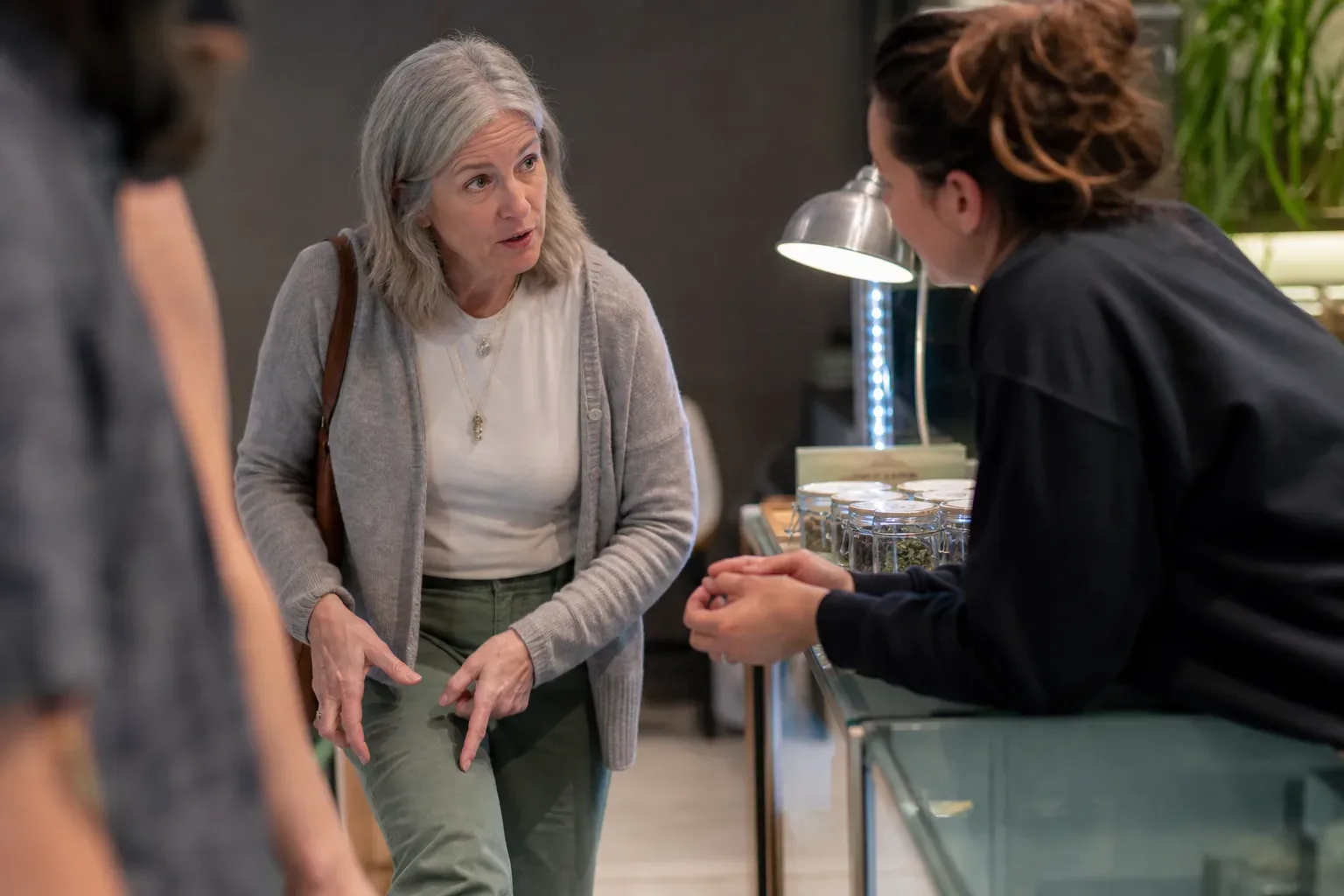 A patient speaking with a budtender and gesturing to their knee area while explaining their condition at a counter