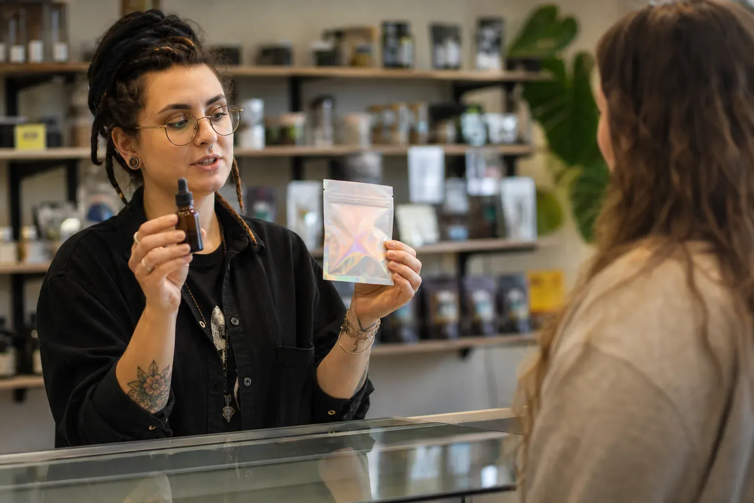 A budtender holding up two different product types—a tincture bottle and an edible package—for a customer to compare