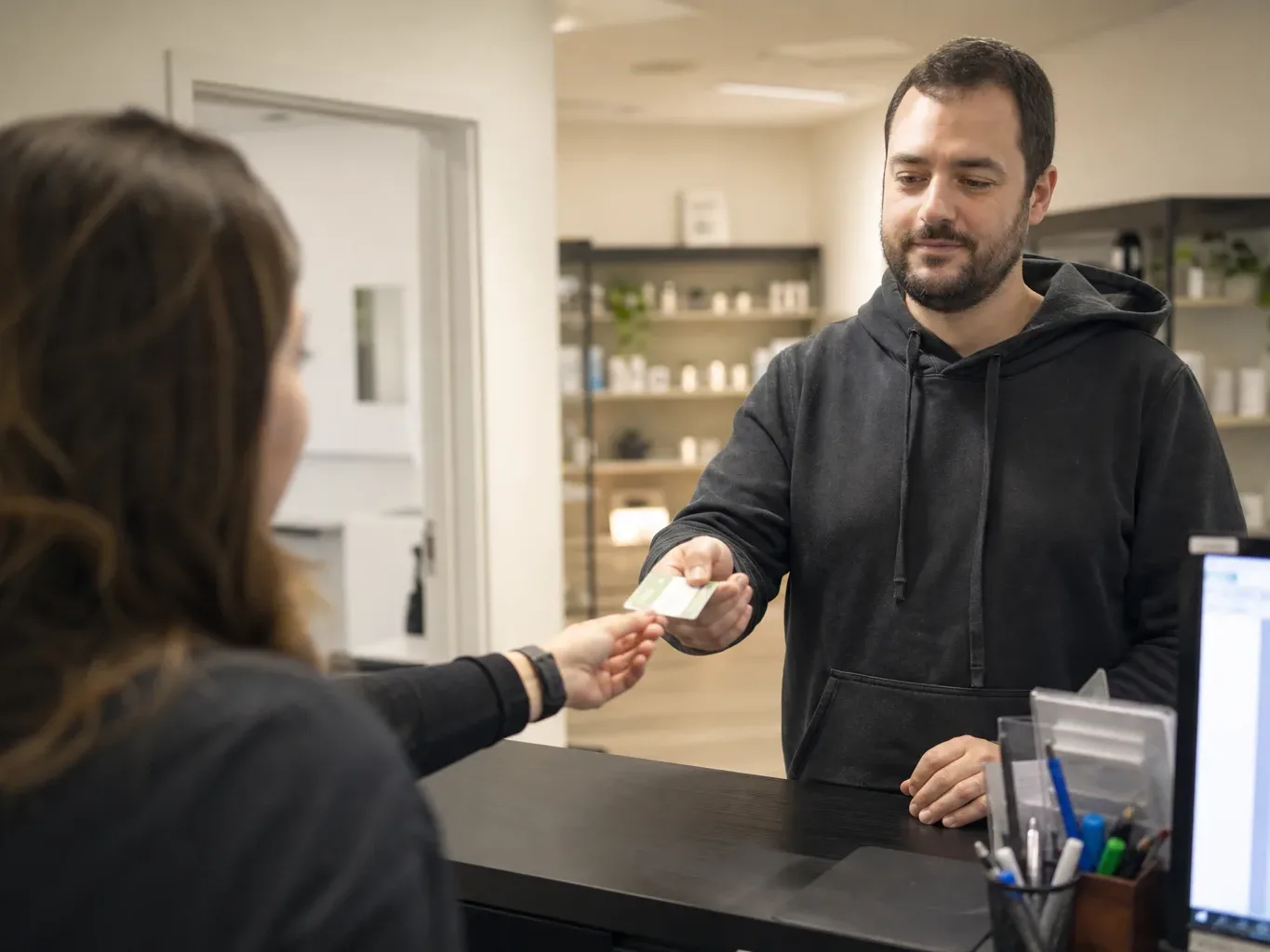 A medical patient handing a laminated medical card to a dispensary staff member at a checkout desk