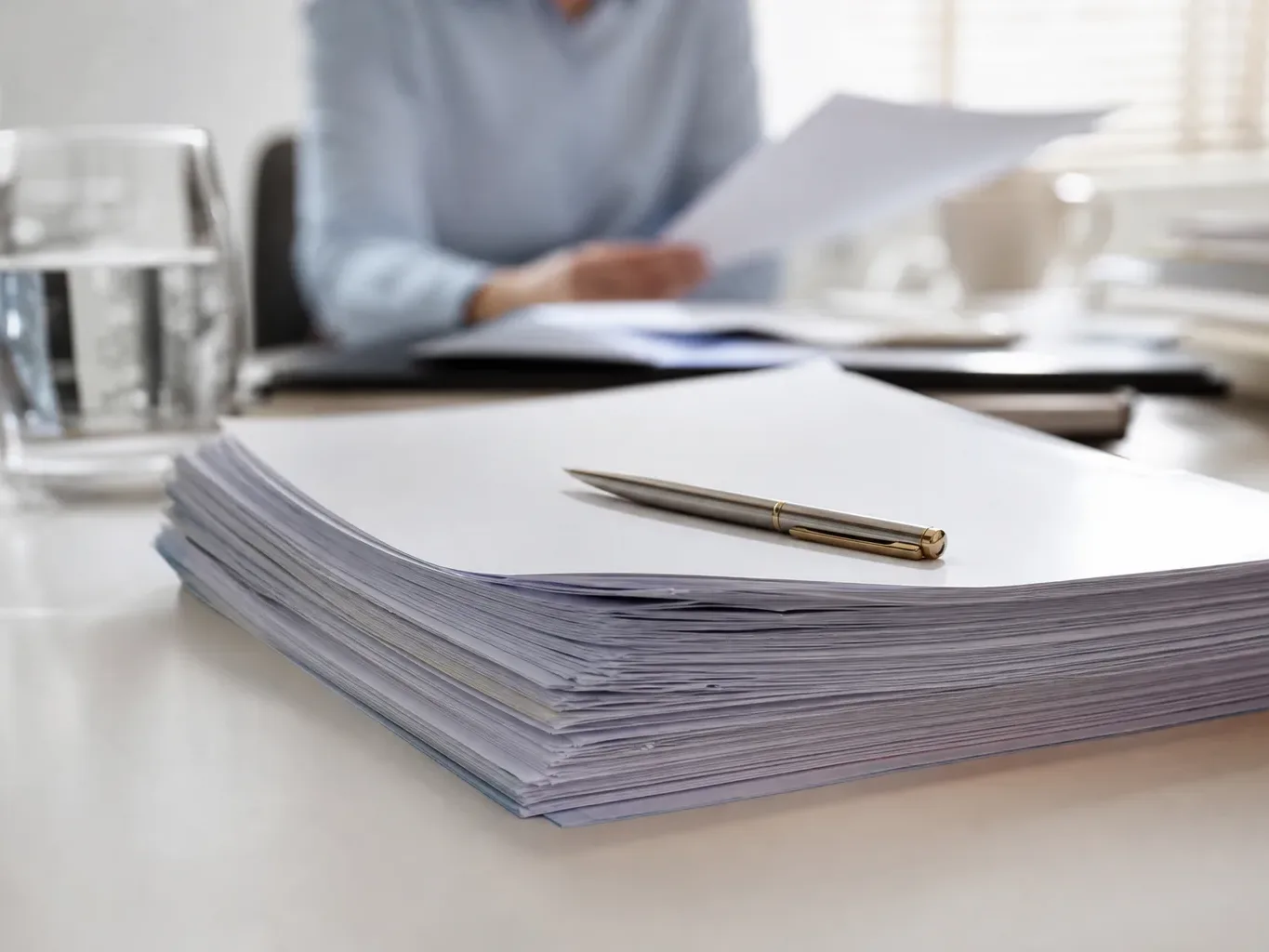 A stack of generic official-looking documents with a pen resting on top on a clean desk surface