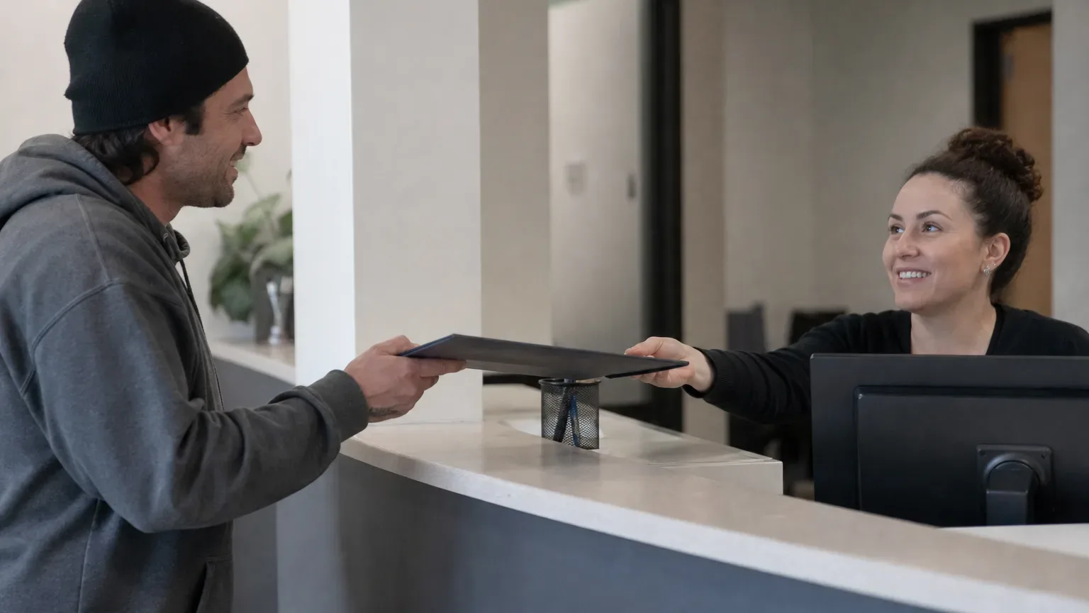 A patient handing a medical documentation folder to a dispensary intake specialist at a front desk